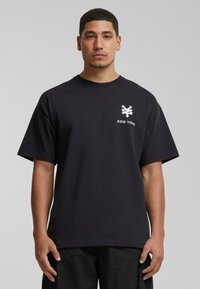 Svart bomulls T-skjorte med rund hals, korte ermer og en hvit Zoo York-logo trykket på venstre bryst. Enkel, rett design.