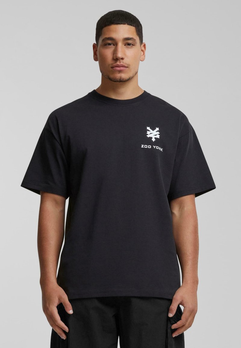 Svart bomulls T-skjorte med rund hals, korte ermer og en hvit Zoo York-logo trykket på venstre bryst. Enkel, rett design.