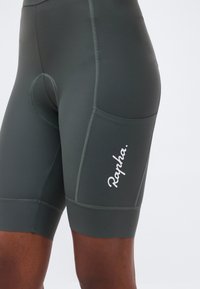 Κοντινή λήψη σκούρων γκρι ποδηλατικών σορτς με πλευρική τσέπη και λευκό λογότυπο "Rapha." στον μηρό.