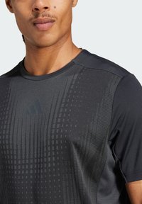 T-shirt de sport noir avec un motif texturé, col rond et logo subtil au centre. Fabriqué en tissu synthétique respirant.