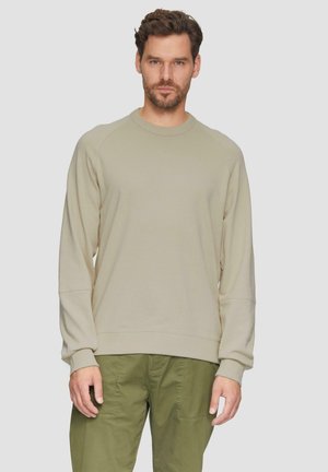 Beige sweatshirt with raglan sleeves, ribbed crew neck, and cuffs. Soft texture with minimal stitching detail. Paired with green pants.