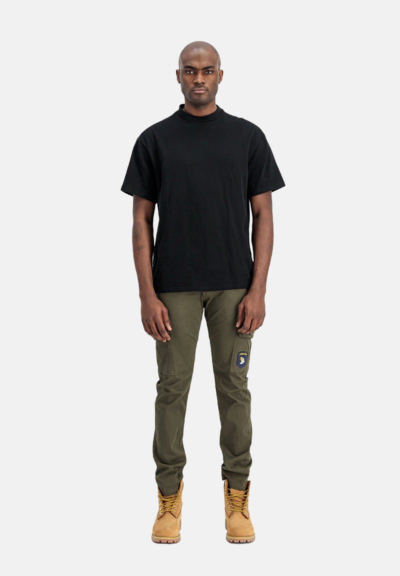 Sort bomulds T-shirt, slim-fit olivenfarvede cargo bukser med sidelommer og brune støvler med snørebånd. Enkel, funktionel design med holdbare materialer.