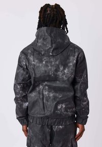 Giacca zip-up tie-dye nera e grigia con un grande cappuccio, polsini e orlo elasticizzati, caratterizzata da una finitura in tessuto testurizzato.