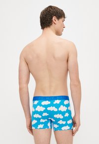 Μπλε μποξεράκια με λευκά σύννεφα, που έχουν μια μονόχρωμη μπλε μέση με την επιγραφή "HAPPY". Μαλακό ύφασμα με άνετη εφαρμογή.