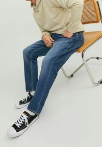 Blå denimjeans med rak passform och synlig sömnad, tillsammans med svarta canvasklackar med vita snören och gummisula.