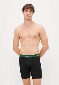 Črne bokserice z elastičnim pasom z zelenim logotipom Lacoste, narejene iz raztegljivega materiala, zasnovane za tesno prileganje.