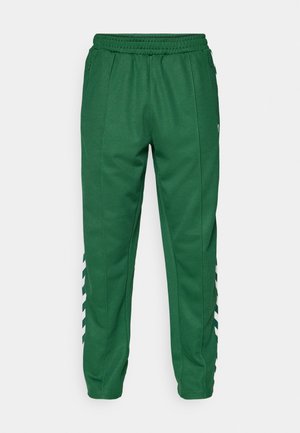 Pantalons de sport verts avec une taille élastique, des poches latérales et des rayures blanches inclinées sur les côtés inférieurs. Texture de tissu lisse.