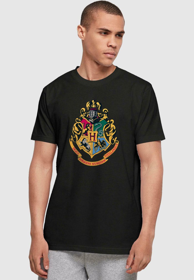 Camiseta de algodón negra con un diseño de escudo colorido que incluye una "H" prominente, acentos dorados y texto en latín sobre un fondo contrastante.