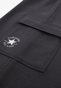 Μαύρο fleece ύφασμα με εμφανή εμπρόσθια τσέπη και λευκό κυκλικό λογότυπο που απεικονίζει ένα αστέρι και το κείμενο «Converse All Star».