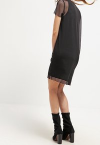 Svart kort klänning med genomskinliga nätärm och nederkant, med en lös passform. Matchad med knähöga svarta tygstövlar.