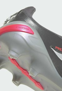 Botín de fútbol con parte superior negra, suela gris y detalles Strikeframe rojos, con tachones redondeados para mayor tracción.