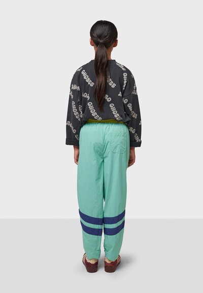 Grauer Pullover mit "CHOOSE"-Druck, kombiniert mit mintgrünen Hosen mit marineblauen Streifen. Modell steht mit dem Rücken zur Kamera, Haar im Pferdeschwanz frisiert.