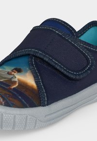 Baskets pour enfants bleu marine avec semelle blanche, doublure bleue et fermeture velcro, avec un joueur de football de dessin animé imprimé sur l’avant.