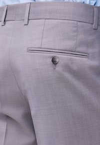 Κοντινό πλάνο ενός ατόμου που φοράει ανοιχτό γκρίζο παντελόνι ελαφρού υφάσματος με μια πιεστήρα κουμπωμένη στην πίσω τσέπη και μπλε πουκάμισο κρυμμένο μέσα.