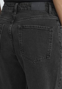 Mustad teksapüksid kõrge vöökohaga, millel on kaks tagataskut ja vöörihmale kinnitatud ristkülikukujuline nahkmärk, millel on kiri "PULZ JEANS".