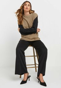 Sweater beige a maglia grossa sovrapposto a una maglietta nera a maniche lunghe, abbinato a pantaloni neri a gamba larga e scarpe col tacco nere.
