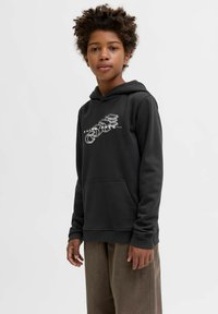 Felpa nera con cappuccio e tasca frontale, caratterizzata da una stampa grafica bianca e un tessuto morbido. Il modello indossa pantaloni beige larghi per un contrasto.