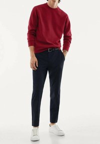 Felpa rossa, pantaloni blu scuro e sneakers bianche. La felpa ha un col tondo; i pantaloni sono slim-fit con una texture liscia.