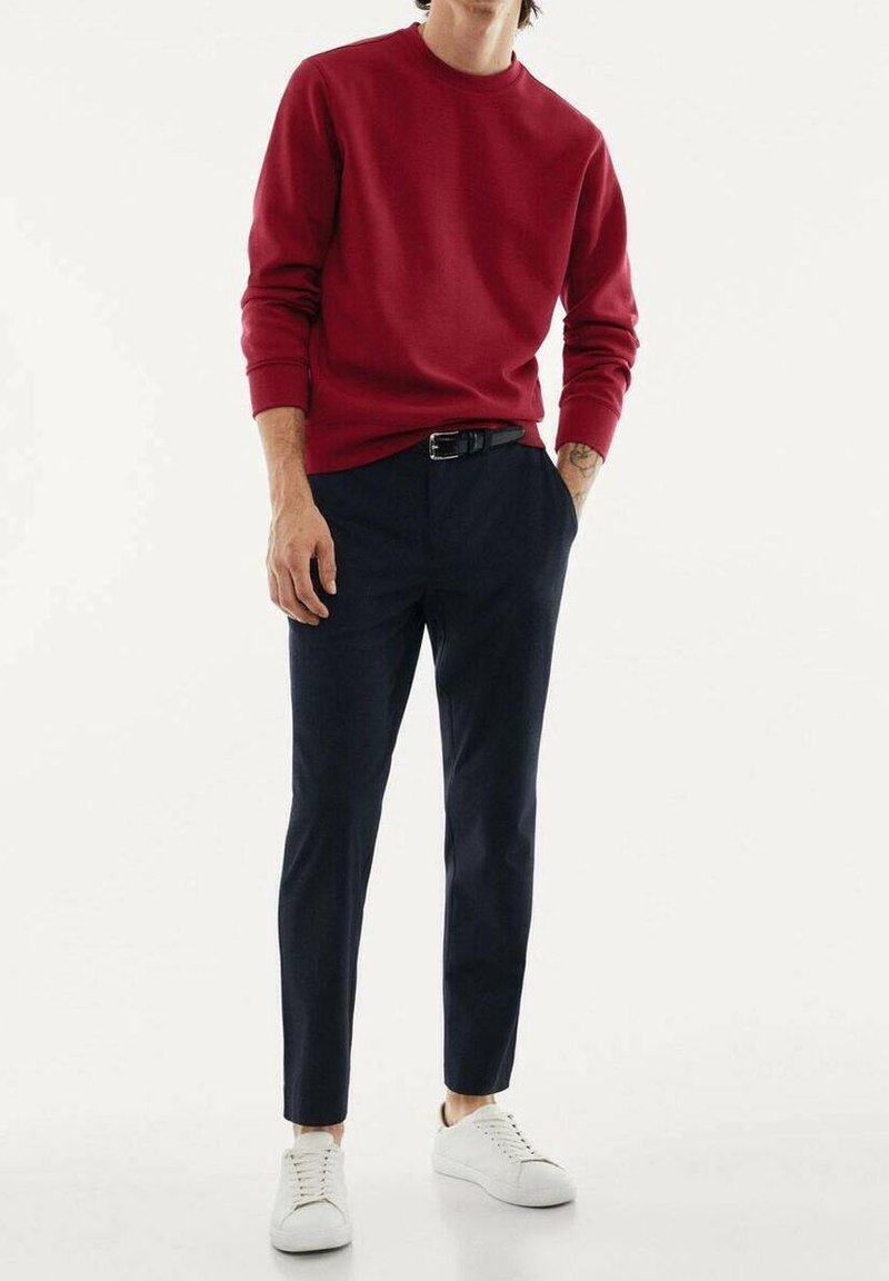 Felpa rossa, pantaloni blu scuro e sneakers bianche. La felpa ha un col tondo; i pantaloni sono slim-fit con una texture liscia.