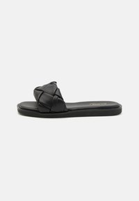 Sandalo slide nero con una cinghia intrecciata e imbottita, suola piatta e design minimalista. Il materiale sembra essere in finta pelle. Nessuna ferramenta visibile.