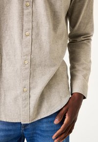 Lichtgrijze visgraat overhemd met beige knopen, met een ronde zoom en lange mouwen, gedragen over blauwe denim jeans.