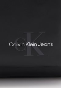 Logo di Calvin Klein Jeans in un materiale nero elegante e in rilievo, con un testo bianco "Calvin Klein Jeans" ben in evidenza e un sottile design "CK" più grande.