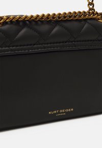 Czarna skórzana torebka Kurt Geiger z pikowanym górnym sektorem i złotym łańcuszkiem na białym tle.
