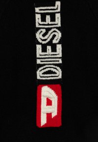 Tessuto a maglia verticale con la parola "DIESEL" in lettere bianche su sfondo nero e un quadrato rosso con una lettera "A" stilizzata in bianco.