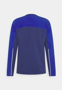 Camicia a maniche lunghe in diverse tonalità di blu con una finitura testurizzata, caratterizzata da un collo rotondo e accenti riflettenti lungo le maniche.