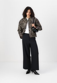 Veste matelassée à imprimé léopard avec un design court, associée à un pantalon large noir, un sac à main noir et des escarpins noirs pointus.