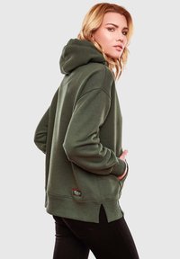 Sudadera verde oliva de tejido suave, con un corte holgado, aberturas laterales y un bolsillo frontal. Los puños y el dobladillo acanalados ofrecen comodidad.