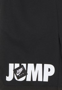 Schwarzer Stoff mit großer weißer Aufschrift "JUMP" und einem Etikett mit dem "JUMP MAN"-Logo, das eine glatte Textur und ein lässiges Design zeigt.