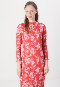 Abito aderente a maniche lunghe di un vivace rosso con un motivo floreale rosa e bianco. Tessuto texturizzato con scollatura rotonda e polsini arricciati.