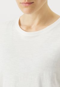T-shirt blanc à manches courtes avec un col rond, fabriqué en tissu léger et légèrement texturé, offrant une coupe douce et décontractée.
