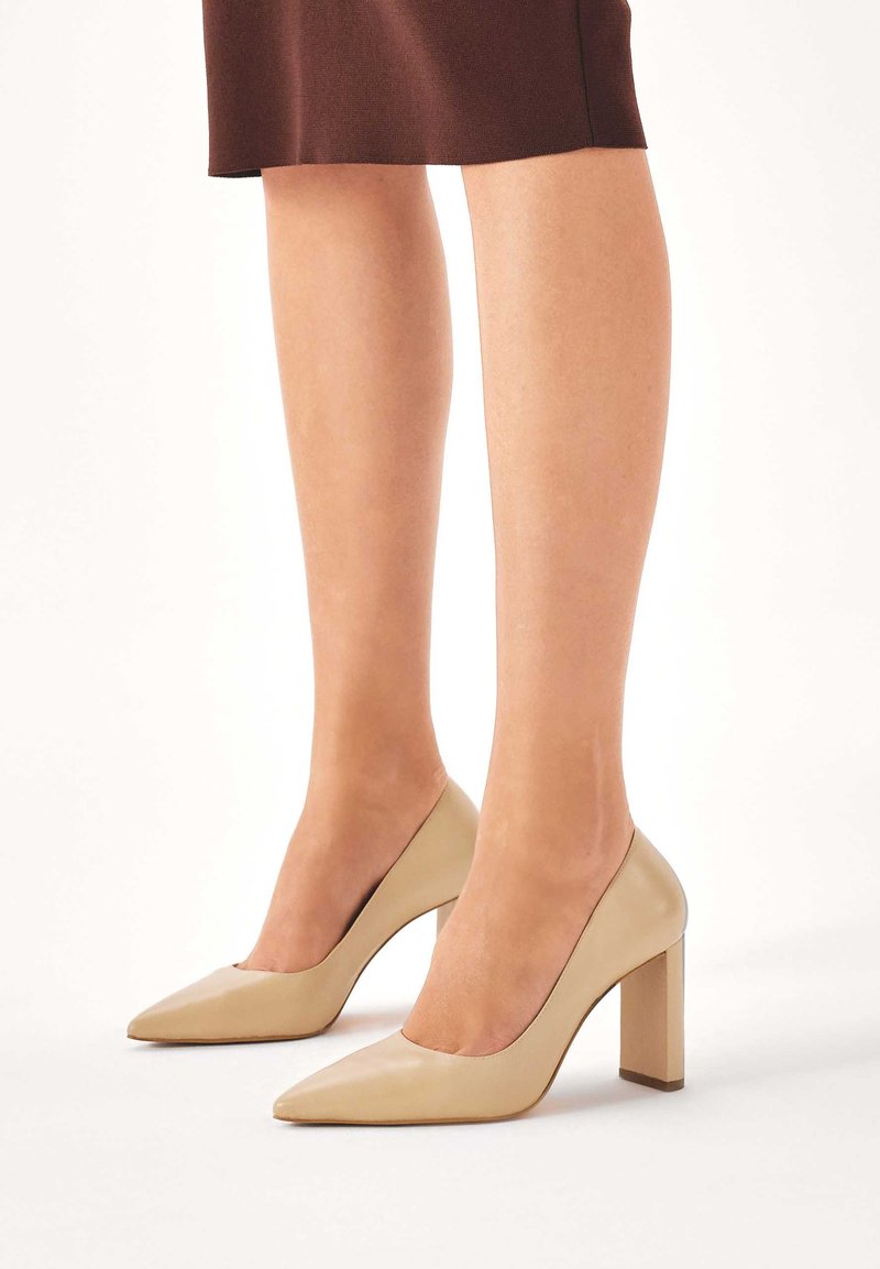 Décolleté beige con punta affusolata in pelle liscia, con tacco largo a blocco e un design pulito e minimalista senza decorazioni visibili.