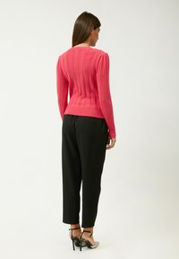 Aansluitende roze geribbelde trui met lange mouwen, gestructureerde stof en een ronde halslijn, gedragen met zwarte tapered broek en hoge hakken.