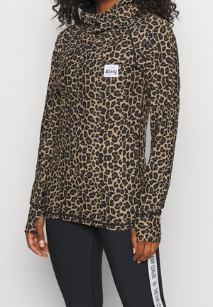 Kvinde iført en brun og sort leopardprint langærmet top med tommelfingerhuller og sorte leggings med hvide sidelommer.