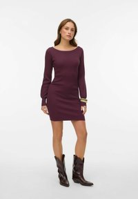 Ribiņš, garām piedurknēm kleita dziļā bordo krāsā ar laivas veida kakla izgriezumu un piegulošu siluetu. Valkāta kopā ar tumši krāsotiem, asa purngala kovboju zābakiem.