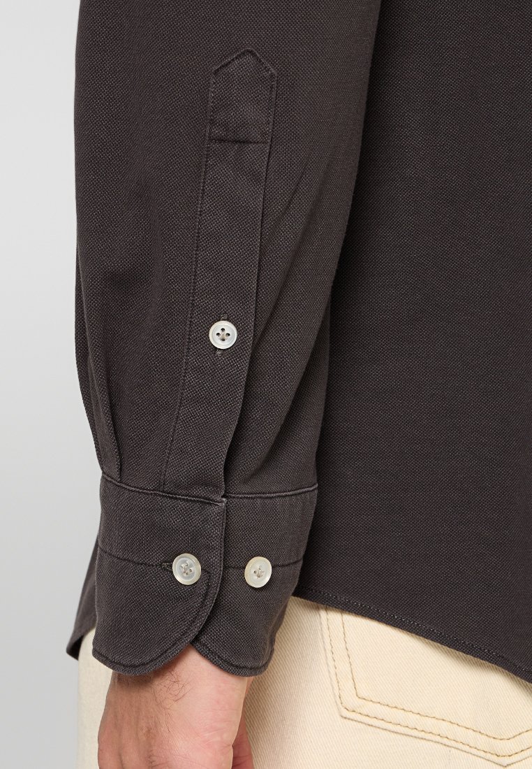 Donkergrijze lange mouwen shirtmanchet met twee witte knopen, gedragen door een persoon in lichtbeige broek.