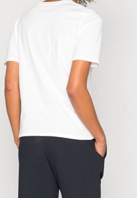 Camiseta de algodón blanca de manga corta con cuello redondo, textura suave y corte holgado, combinada con pantalones oscuros de corte ancho.