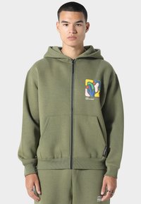 Oliven grøn zip-up hættetrøje lavet af blødt stof, med grafisk design på venstre bryst, kengurulommer og ribbede manchetter.