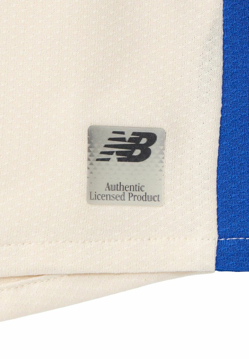New Balance Markenetikett mit dem Text "Authentic Licensed Product" am Saum eines cremefarbenen und blauen Stoffkleidungsstücks.