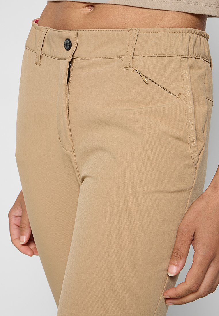 Beżowe spodnie o gładkiej strukturze, elastycznym pasie, przednim zamku błyskawicznym i bocznej kieszeni. Zawierają subtelne logo wzdłuż szwu bocznego.