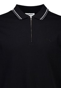 Svart polo t-shirt med dragkedja i kragen, med vita och grå ränder. Inkluderar diskret logobroderi på bröstet och texturerad tyg.