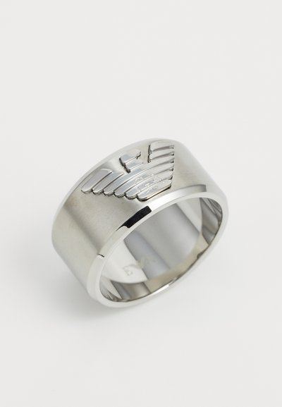 Kroužek z nerezové oceli s vyvýšeným designem křídla, leštěný povrch a široký pás. Hladká textura s vyrytými detaily na jedné straně.