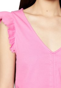 Růžový žebrovaný top s výstřihem do V a volánkovými rukávy. Má texturovanou látku a bezešvý design v oblasti výstřihu.