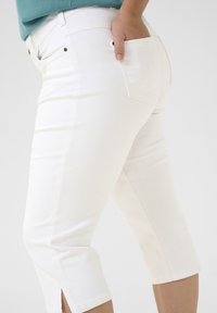 Pantalones blancos cortos de corte ajustado, con bolsillos traseros y aberturas en los laterales del dobladillo. Fabricados con un material suave y elástico.