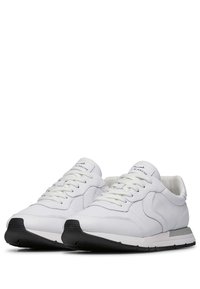 Weiße Leder-Sneaker mit strukturierten Akzenten, einer schwarzen Gummisohle, flachen Schnürsenkeln und einem Logo auf der Zunge. Klassisches sportliches Design.