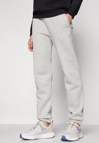 Grau Sweatpants aus einem weichen Material, mit seitlichen Taschen und elastischen Bündchen. Dazu leichte Laufschuhe in Grau, Orange und Blau.