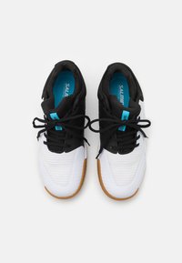 Zapatillas deportivas en blanco y negro con una parte superior de tela texturizada, suela de goma y acentos en azul. Los cordones están atados, lo que revela un cuello acolchado.